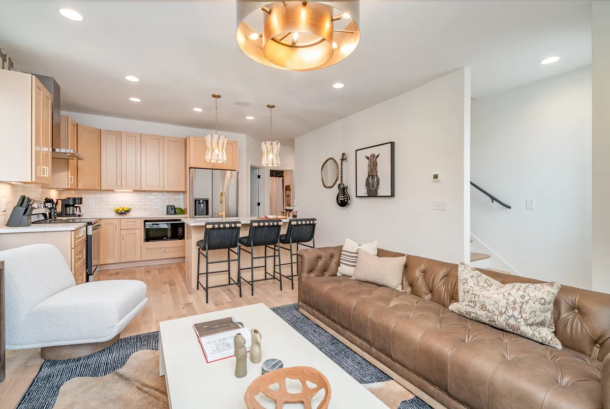 A welcoming, contemporary living space with a chic leather sofa, a stylish kitchen island, and modern light fixtures. The arrangement encourages group interaction, whether for family meals, game nights, or relaxed lounging.