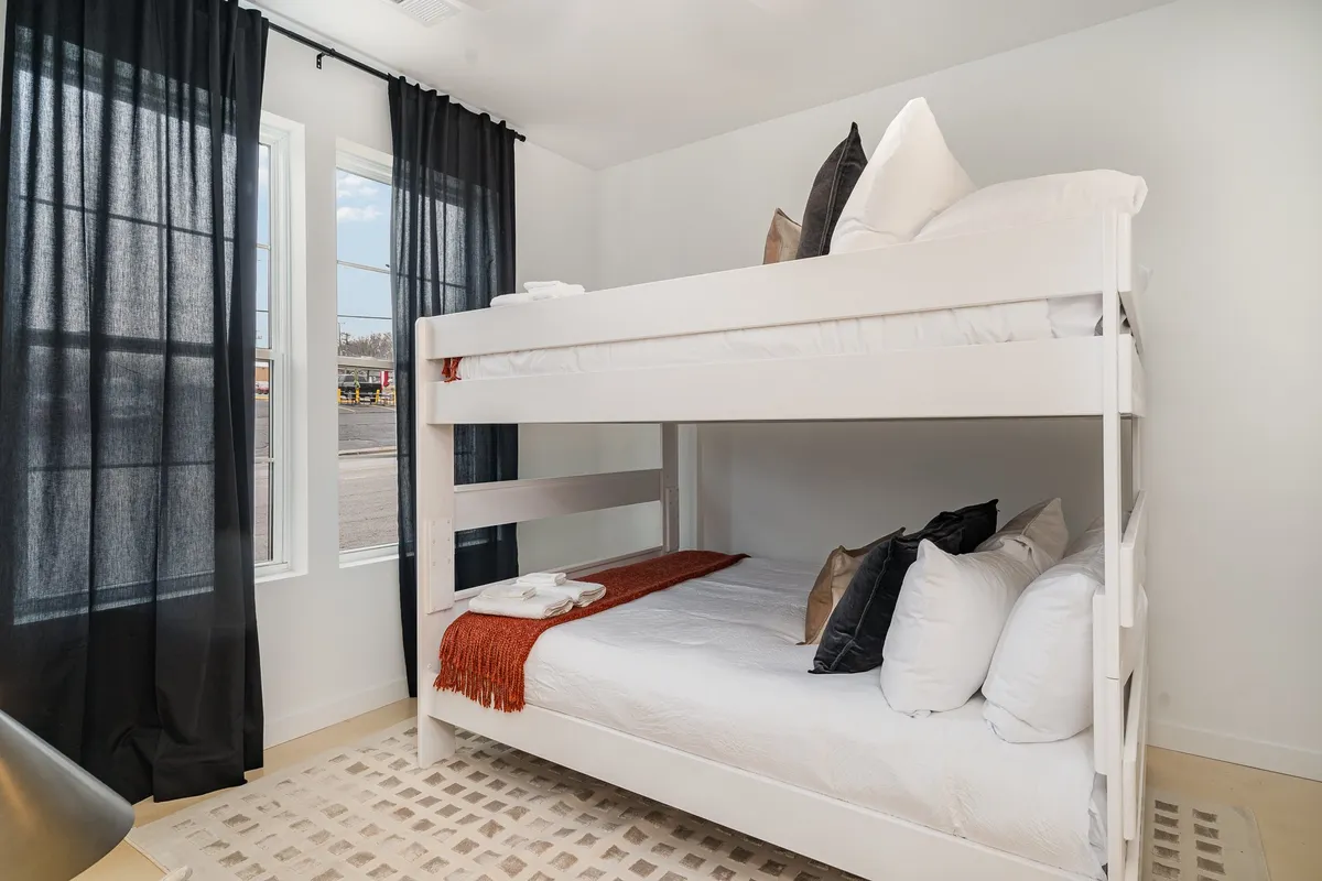 A playful bunk bed setup with black curtains and a cozy textured rug, evoking a sense of fun and comfort for younger guests or groups looking for a relaxed, communal atmosphere. The space is inviting for bedtime stories and shared moments.