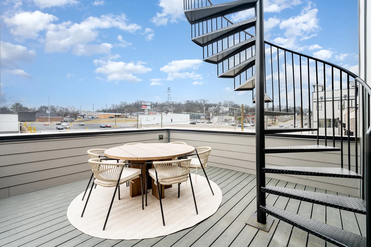 Featuring a spiral staircase leading up to a spacious rooftop terrace, this image highlights an outdoor dining table and comfortable seating. The mood is inviting and relaxed, with plenty of room for group gatherings, celebrations, or intimate dinners against the open sky.