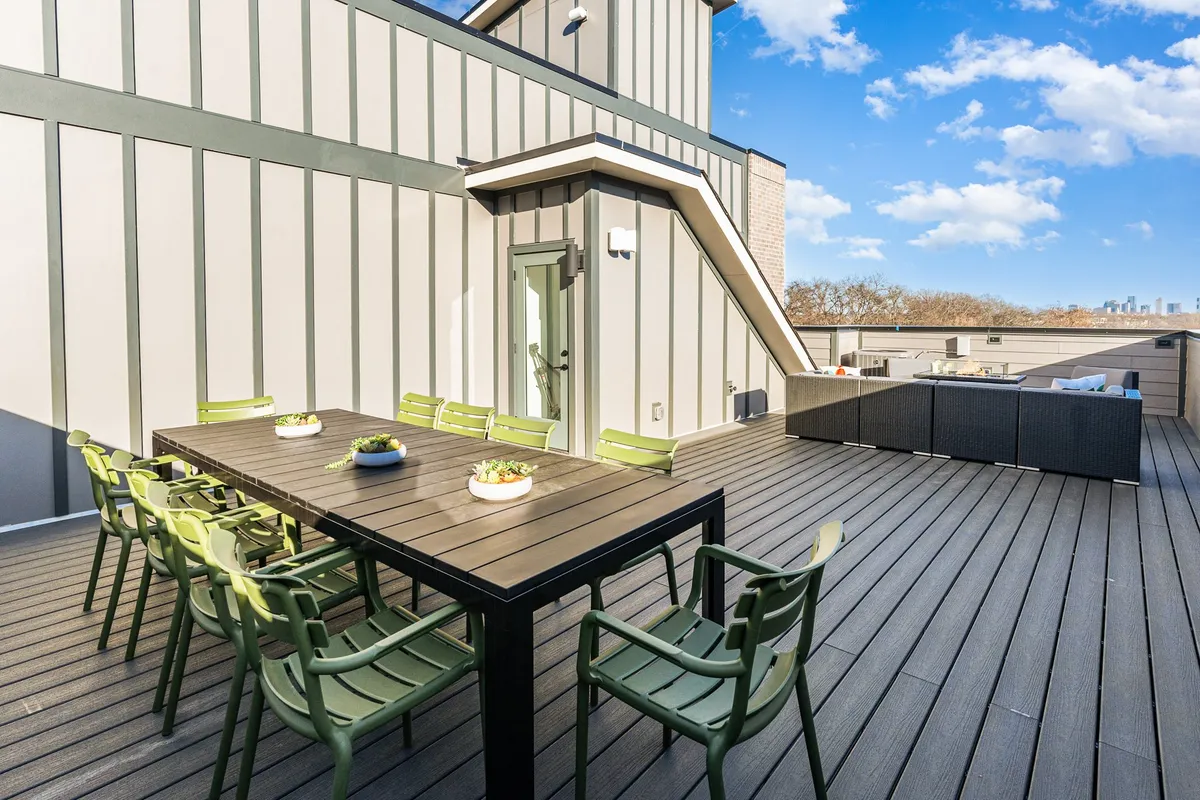 This rooftop patio features a large dining table surrounded by green chairs, all set against a stunning backdrop of the Nashville skyline. The space is perfectly suited for outdoor dining, group gatherings, and taking in sunset views over the city.