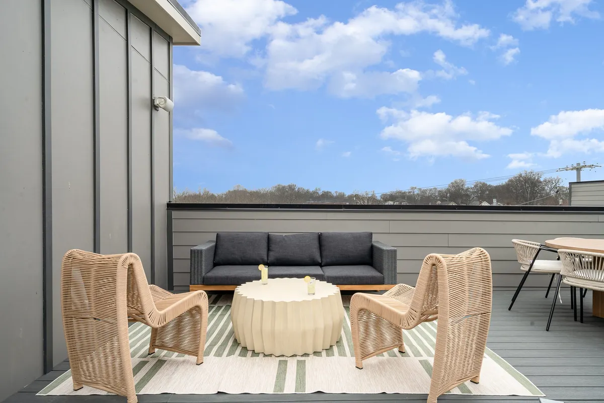 A spacious rooftop patio furnished with wicker chairs, a round coffee table, and a sofa, suggesting a comfortable outdoor setting perfect for group gatherings. The area is designed for socializing, relaxing, and entertaining, with enough space for everyone to spread out and enjoy sunset views or morning coffee together.