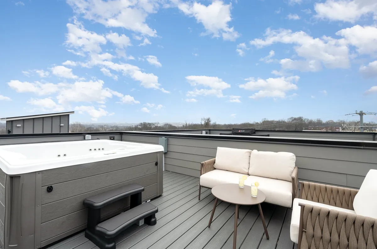 A tranquil rooftop patio with a bubbling hot tub, outdoor seating, and scenic city views. The ambiance suggests relaxation, stargazing, and enjoying a warm soak with friends or family.