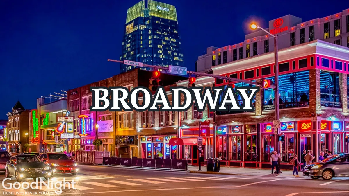 A lively Nashville street scene at night featuring glowing neon signs, bustling sidewalks filled with people, and buildings illuminated by colorful lighting. The atmosphere is energetic, hinting at live music venues, dining spots, and honky-tonk bars lining the avenue.