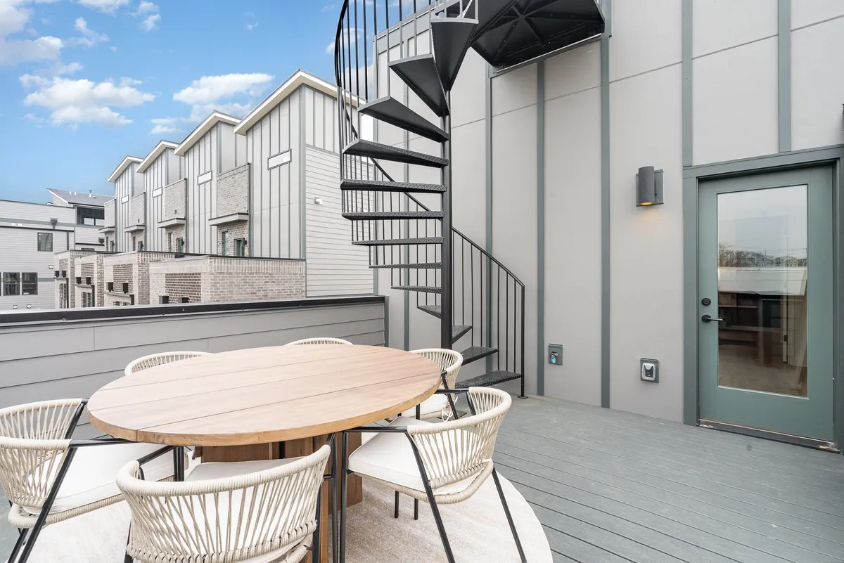 An inviting exterior rooftop setup displays a dining table and outdoor seating, with surrounding buildings visible in the distance. The scene is casual yet chic, ideal for sunset dinners, starlit conversations, or celebratory toasts among friends and family.