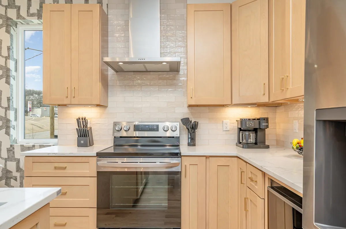Focused on the kitchen, this image features a stainless steel stove, modern hood, wooden cabinetry, countertop with a fruit bowl, and a coffee machine. The area is bright and functional, inviting guests to cook or gather around meal prep.